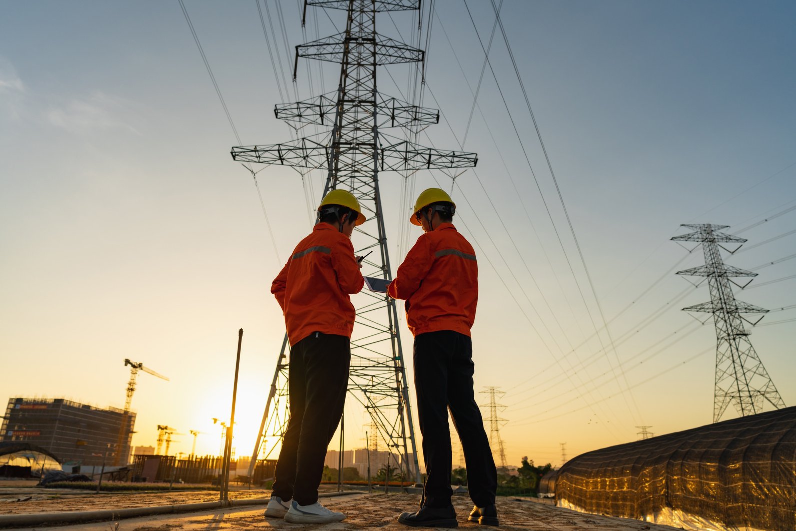 Two electric workers using tablet computer at sunset